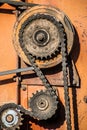 Old oiled chain system with a rusty industrial sprocket on an orange harvester with shadows
