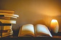 An old open book with blank pages on a candle lit table next to a stack of books Royalty Free Stock Photo