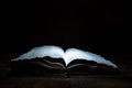 An old open book is lying on a wooden table in the dark. A light shines on the book from above. Holy Bible. Royalty Free Stock Photo