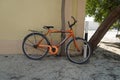 An old orange bicycle is standing on the sand path locked to a tree. Old Apache orange cycle chained to a tree. Man`s Cycle with