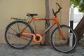 An old orange bicycle is standing on the sand path locked to a tree. Old Apache orange cycle chained to a tree. Man`s Cycle with