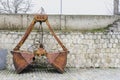 Old orange and rusty Crane bucket in front of a wall.