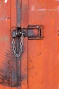 Old orange rusty iron door with lock, metal parts, bolt, nuts and shiny chain. Selective focus Royalty Free Stock Photo