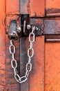 Old orange rusty iron door with lock, metal parts, bolt, nuts and shiny chain. Selective focus Royalty Free Stock Photo