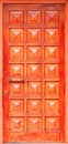 Old orange wooden entrance doors with a bronze handle and symmetrical square panels in Greek style