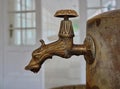 Old ornamental metallic spring water tap with water drop at faucet mouth and white door in the background Royalty Free Stock Photo