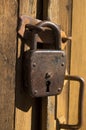 An old padlock rusty weighs on a wooden door.