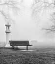 old park bench in the morning winter fog in the park with trees and old monument Royalty Free Stock Photo