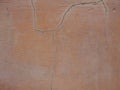 Old peeling red terracotta pink plaster on a cracked rough, scratched uneven concrete stone wall. Royalty Free Stock Photo