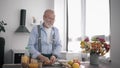 Old peppy man with beard in glasses lover of proper nutrition prepares healthy fruity salati drinks vitamin juice while