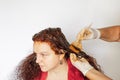 Old person dyeing female hair in red color with help of brush in hands in latex white gloves on white background. Hair