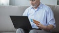 Old person viewing photos of resort town, booking hotel room on laptop at home