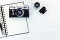 Old photo camera, lens, film roll, notepad and pen on white wood Royalty Free Stock Photo