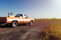 Old pickup truck riding along a farm road with a ranch and horses on the background at sunset in rural Texas