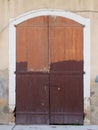 Old picturesque decaying brown painted wooden double doors bolted shut with a padlock set in a white stone frame