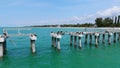 Old pier in state of disrepair with several birds perched on posts and horizontal beams of bridge. Crystal water with
