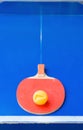 Old pingpong racket and a dented ball on blue pingpong table
