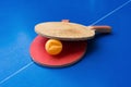 Old pingpong rackets and a dented ball on blue pingpong table