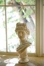 An old plaster sculpture of a man stands on the windowsill. There is a glass window in the background