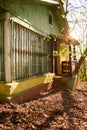Old porch of an abandoned house. ragged yellow paint on the facade, windows with bars. sunlight breaks through tree branches Royalty Free Stock Photo