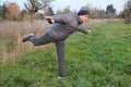 Old positive man in a hat with a smile goes in for sports, performs physical exercises for balance in nature, the concept of a Royalty Free Stock Photo
