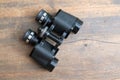 Old prism black color binoculars over wooden background closeup