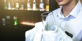 Old pub with bartender cleaning the glass with white towel on background. Empty name tag badge on the shirt uniform. Barman at his Royalty Free Stock Photo