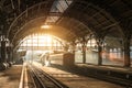 Old railway station with a train and a locomotive on the platform awaiting departure. Evening sunshine rays in smoke arches Royalty Free Stock Photo