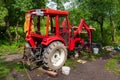 An old red agricultural tractor stands in the forest during repairs and maintenance with the wheel removed and the dismantled