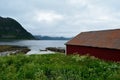 Old red boat house with cloudy mountain range background and small docked boat Royalty Free Stock Photo