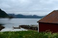 Old red boat house with cloudy mountain range background and small docked boat Royalty Free Stock Photo