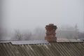 Old red brick chimney on a roof covered with corrugated asbestos-cement sheet, autumn foggy rural landscape Royalty Free Stock Photo