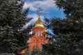 Old red brick Christian church with golden and gilded domes against a blue sky and tree branches. Concept faith in god, orthodoxy Royalty Free Stock Photo