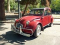 old red burgundy popular Citroen 3CV 1960-1979 in the street in front of a park. Classic car show.