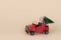 Old red car carrying Christmas tree on beige background. Creative Holiday idea Royalty Free Stock Photo