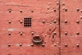 An old red door of medieval style with metallic rivets, heart shaped keyhole plate, cast iron knocker and wire mesh spyhole