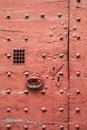 An old red door of medieval style with metallic rivets, heart shaped keyhole plate, cast iron knocker and wire mesh spyhole