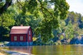 Old red house standing in quaint contrast to the tranquil waters of Lake Malaren, Sweden.