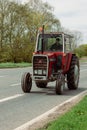 Ely, Cambridgeshire-UK: April 2023: Old red Massey Ferguson 565 tractor being driven on busy main road.