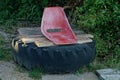 Old red plastic chair on wooden planks and black car tire among green grass Royalty Free Stock Photo