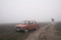 Old red retro car stands in fog near the dirt road, girl in white coat walks under umbrella on the background Royalty Free Stock Photo