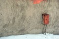 Old red rusty iron electricity box on wall with gray plaster, white snow on the ground Royalty Free Stock Photo