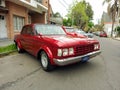 Old red 1970s Falcon four door sedan parked in the street. Classic car show.