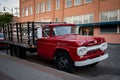 Old red truck with a wooden cargo bed parked by an urban building