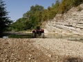 An old red two-seater Quad bike without a driver near a small mountain river on a background of rocks and green trees. Royalty Free Stock Photo