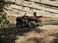 An old red two-seater Quad bike without a driver near a small mountain river on a background of rocks and green trees. Royalty Free Stock Photo