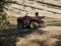 An old red two-seater Quad bike without a driver near a small mountain river on a background of rocks and green trees. Royalty Free Stock Photo