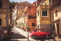 Old Red Vintage Car Italian Scene In The Historic Center Of Small Village In Italy. Elba Island, Marina Di Campo City. Retro