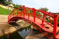 Old red wooden bridge across small river in a green park. Vintage Japanese style bridge is reflected in the water. Uman, Ukraine Royalty Free Stock Photo