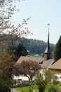 Old reformed church building in Urdorf, Switzerland among trees in spring, lateral view with village shield on the top of he tower Royalty Free Stock Photo